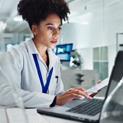 Une femme en blouse blanche, assise à un bureau, tape à l'ordinateur portable