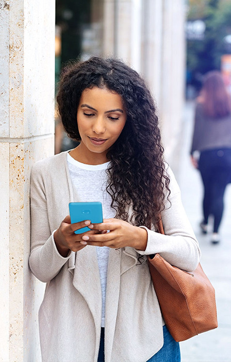Jente sjekker mobilen sin og står ved siden av en søyle